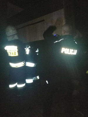 Policjanci wspólnie ze strażakami wynoszą mienie z płonącego domu